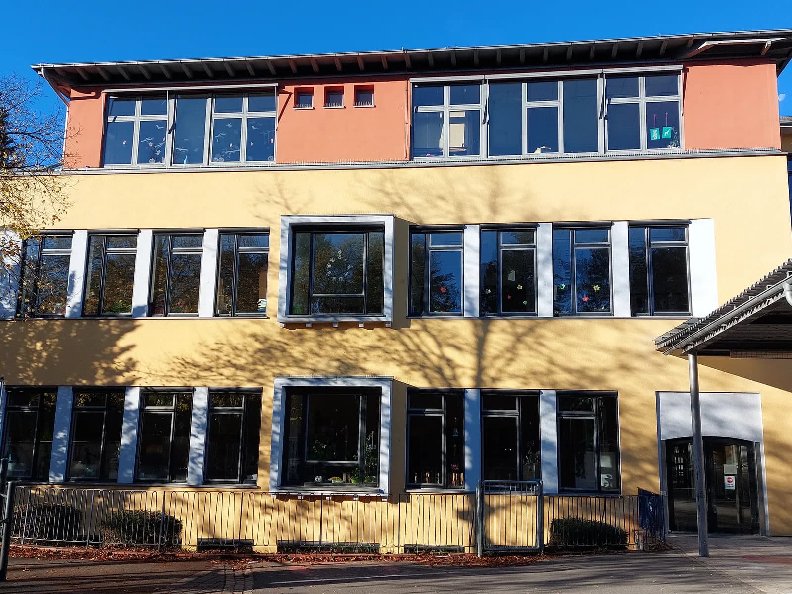 Die Fassade des Hauptgebäudes der Regenbogenschule mit großen Fenstern und blauem Himmel