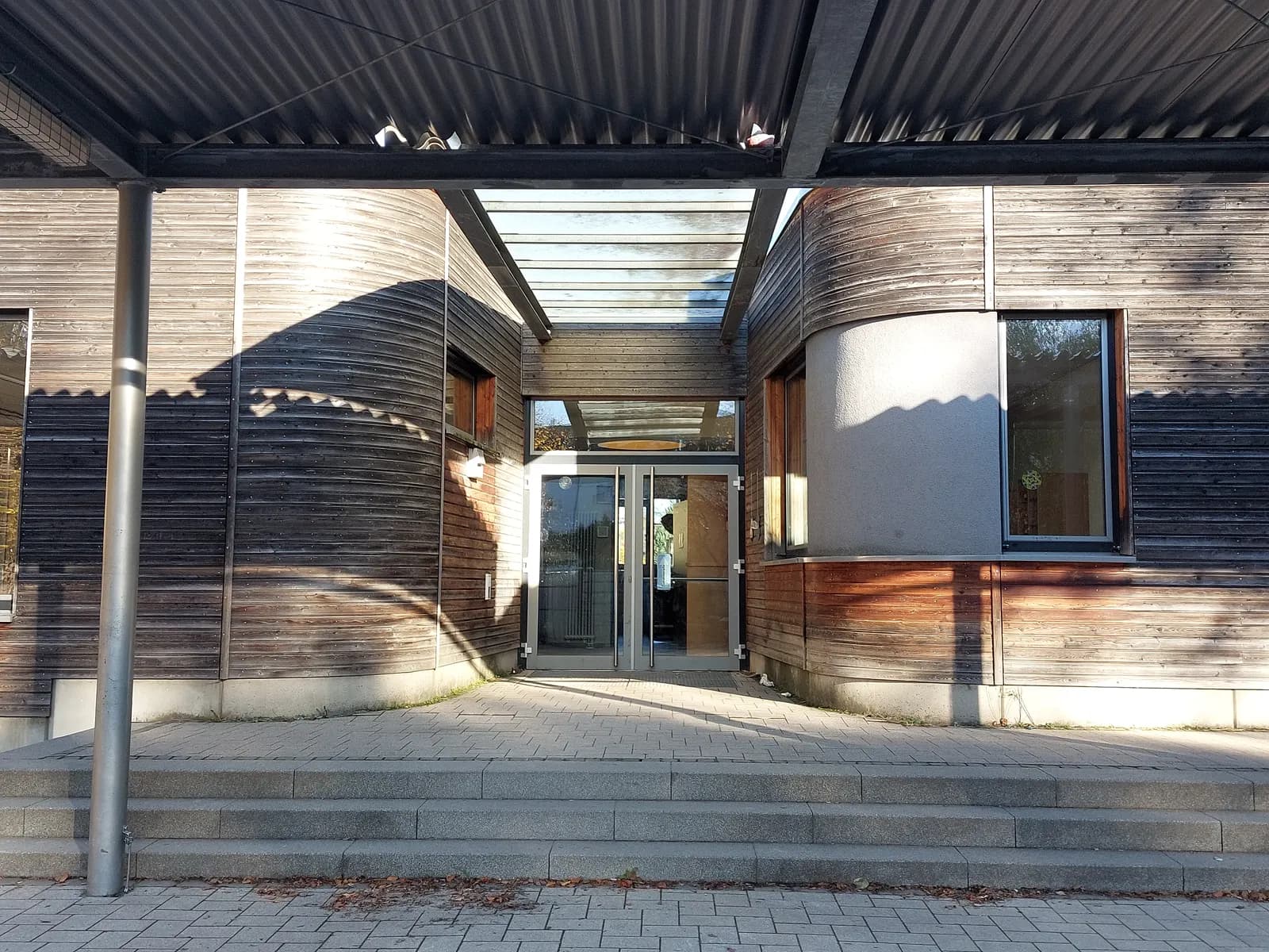 Eingang der Regenbogenschule mit der geschwungenen Holzarchitektur
